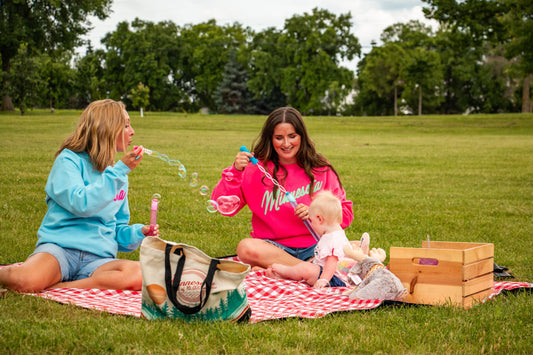 Two women blow bubbles on a picnic blanket and enjoy summer