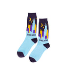 A pair of crew socks with a Chicago skyline graphic on a light blue background, featuring dark purple heels, toes, and cuffs, and yellow crescent moons and stars.