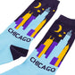 A pair of Chicago-themed crew socks with a light blue lower half, dark purple upper half featuring a skyline and moon and stars, and the word 'CHICAGO'.