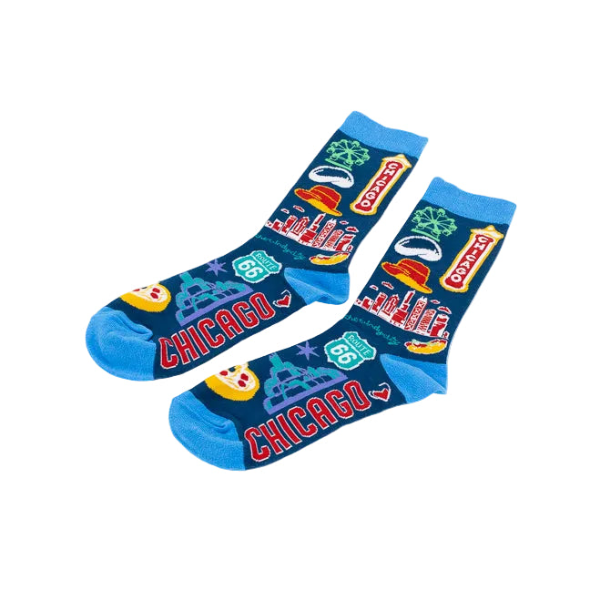 A pair of socks with a vibrant Chicago-themed graphic print on a white background. The socks feature a dark blue base with illustrations of Chicago icons like the skyline, a Ferris wheel, a marquee, a 'CHICAGO' sign, pizza slices, and Route 66 shields, with bright blue cuffs and toes.