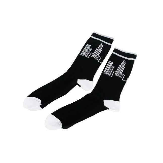 A pair of black crew socks with white toes, heels, and cuffs, featuring a white line-art skyscraper graphic on the upper leg, displayed on a clean white background.