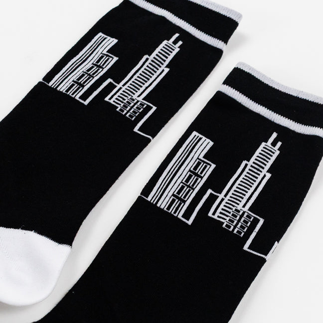 Black crew socks with white ribbed cuffs, white toes, and a white line-art graphic of skyscrapers, shown on a white background.