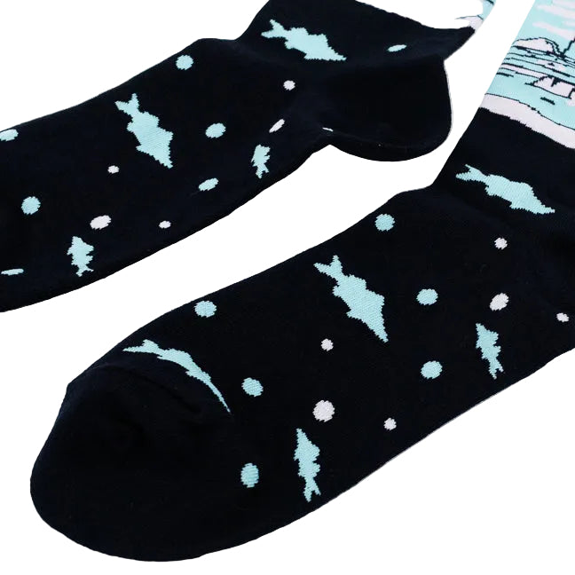 A pair of crew socks on a plain white background. The socks are dark navy with a light blue graphic on the upper calf showing a figure ice fishing with the text 'SURROUNDED BY ICE HOLES', and a lower section with light blue fish and bubbles.