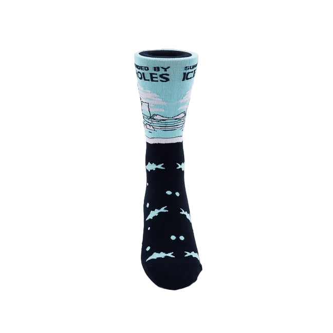 A single crew sock on a white background. The lower half is navy with light blue fish and white dots, while the upper cuff is light blue with a dark silhouette of a fisherman and the text 'SURROUNDED BY ICE HOLES'.