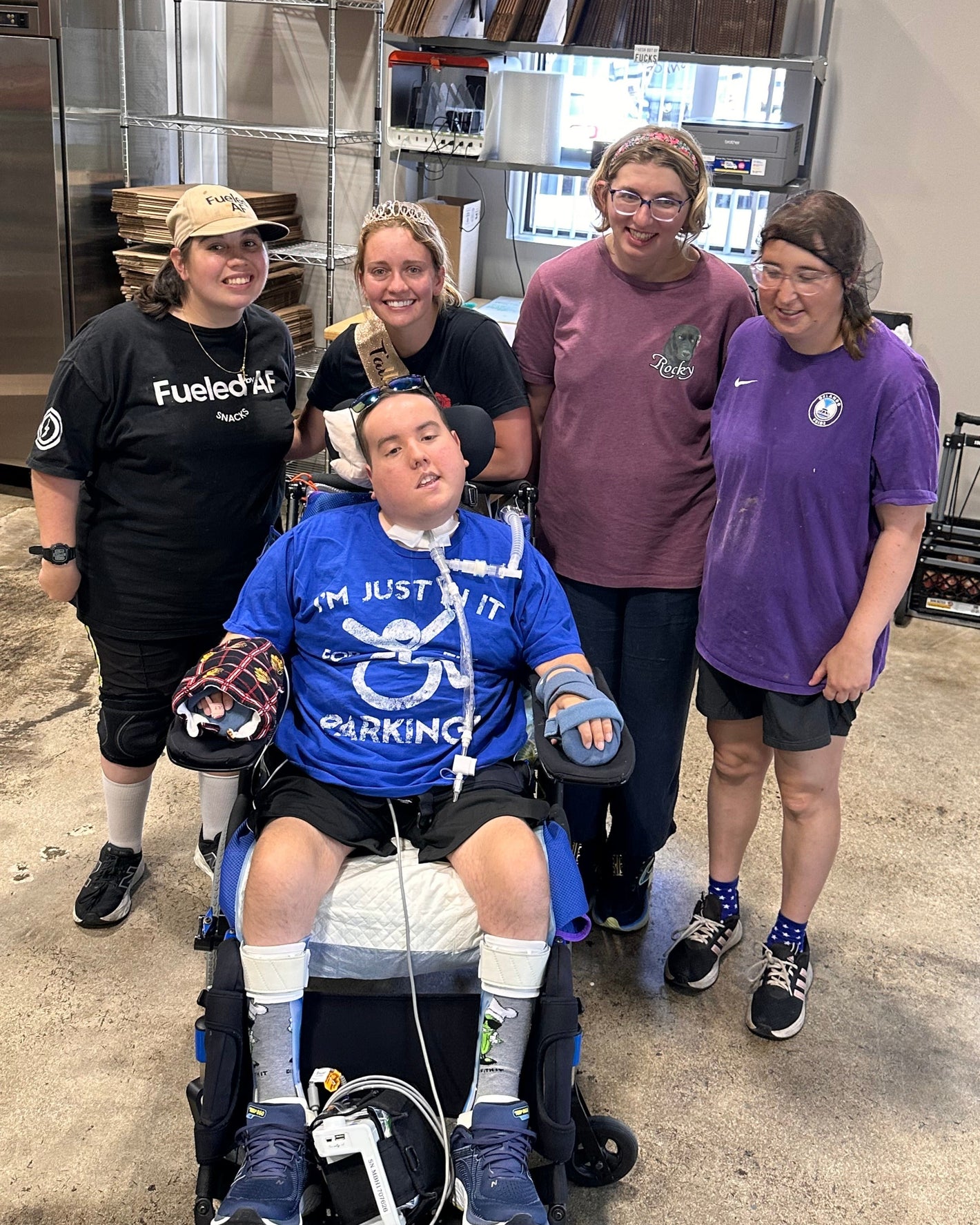 Person in a wheelchair with four support staff members in a warehouse setting