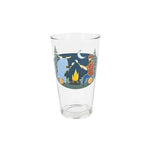A clear glass pint glass featuring a colorful illustration of a campfire scene with Babel the Blue ox, Paul Bunyan, trees, a moon, and a campfire, set against a plain white background.