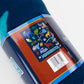 A close-up of a folded dark blue fleece blanket with a colorful Minnesota-themed paper label wrapped around it. The label features Minnesota icons illustrations and the word 'MINNESOTA'.