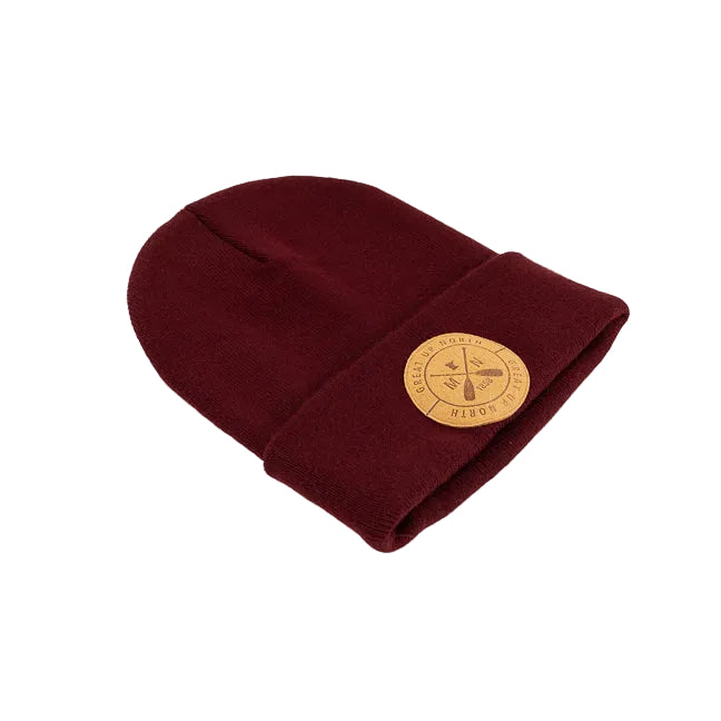 A black knit beanie hat with a folded cuff, featuring a circular tan leather patch on the front with crossed oars and the text 'GREAT UP NORTH' set against a white background.