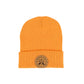 An orange knit beanie hat with a folded cuff, featuring a circular tan leather patch on the front with crossed oars and the text 'GREAT UP NORTH' set against a white background.