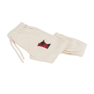 Cream-colored sweatpants with a small red and black graphic patch on the left thigh, displayed on a clean white background.