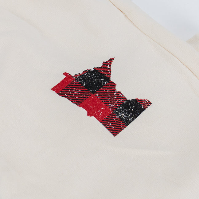 A close-up of a cream-colored sweat pant featuring a printed graphic of the state outline of Minnesota in a red and black buffalo plaid pattern.