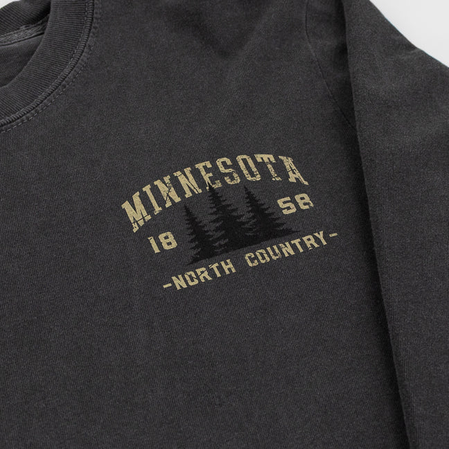 Close-up of a dark charcoal gray long-sleeve t-shirt with a distressed tan graphic on the chest reading 'MINNESOTA 1858 -NORTH COUNTRY-' with pine tree silhouettes.