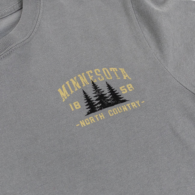 Close-up of a heather gray t-shirt featuring a distressed yellow and black graphic on the chest that reads 'MINNESOTA 1858 -NORTH COUNTRY-' with pine tree silhouettes.