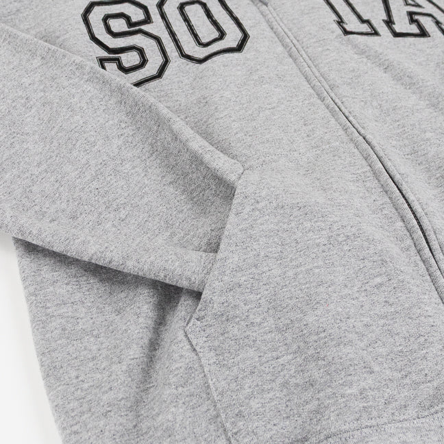 Close-up of a sport gray zip-up hoodie with black outlined varsity-style lettering across the chest and the sleeve tucked inside a front pocket.
