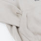 Close-up of a light beige-colored sweatshirt with the sleeve tucked inside a front kangaroo pocket.