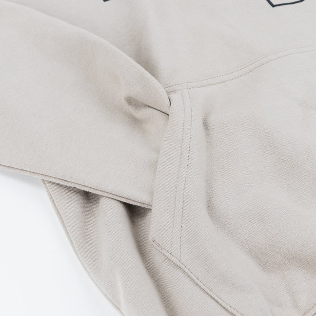 Close-up of a light beige-colored sweatshirt with the sleeve tucked inside a front kangaroo pocket.