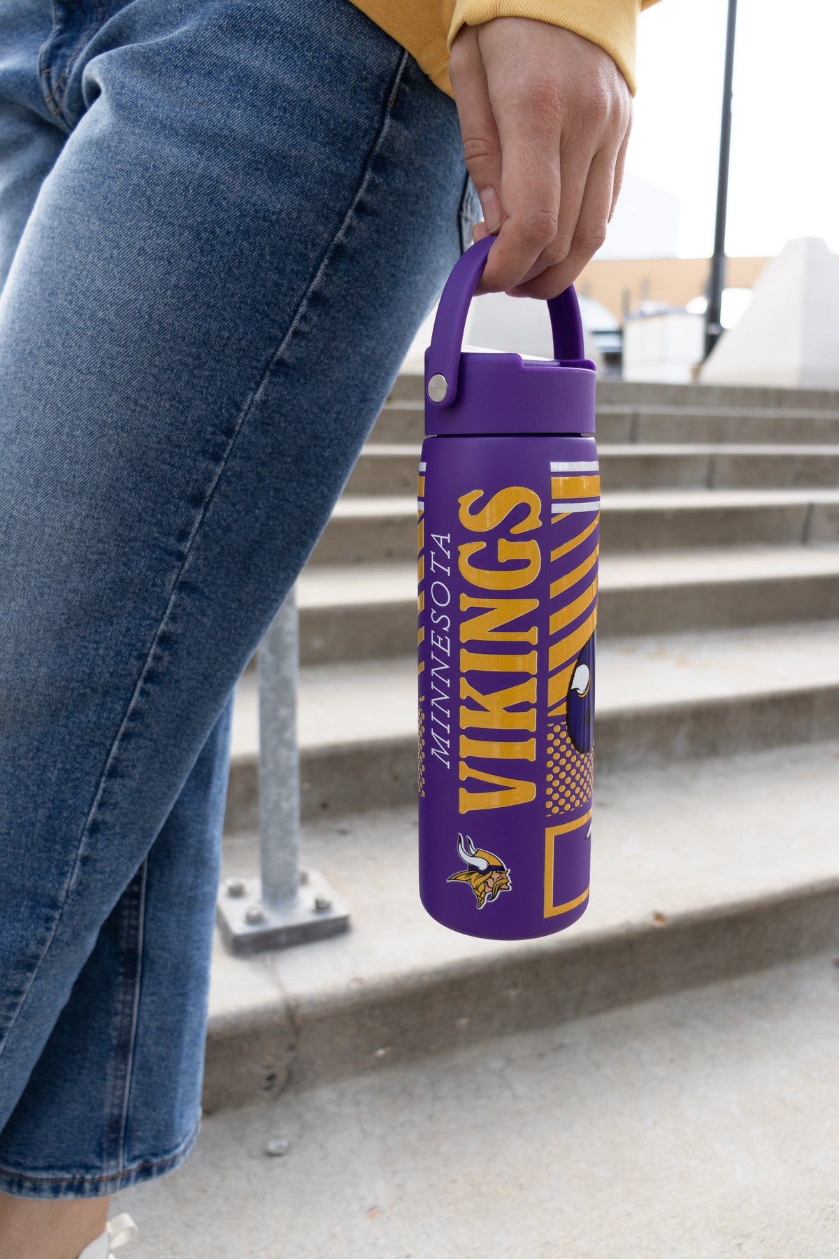 A close-up of a woman holding a purple and yellow insulated water bottle with Minnesota Vikings text and the Minnesota Vikings NFL logo.