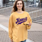 A woman smiles as she walks past a football stadium. She wears a yellow sweatshirt with purple text that reads Minnesota. 