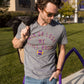 A man wearing a gray graphic t-shirt with purple and yellow text that reads 'WIN OR LOSE WE STILL BOOZE' with a football logo, standing outdoors on a grassy lawn.