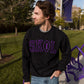 A man stands outside wearing a black sweatshirt with purple letters that reads SKOL. The O in SKOL is in the shape of a football.