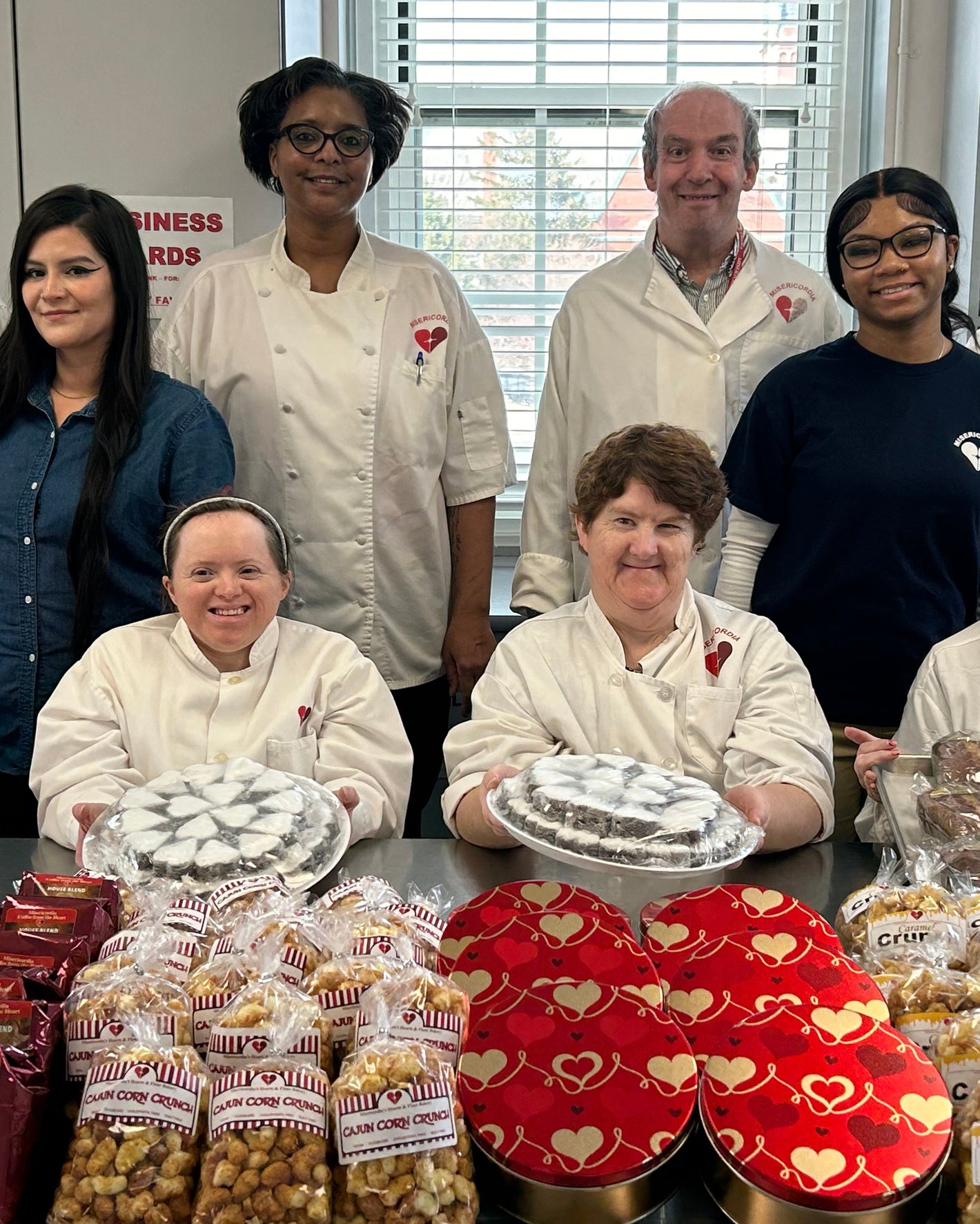 Group of people with baked goods and heart-shaped items in a kitchen setting
