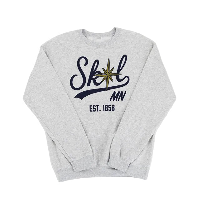 A light heather gray crewneck sweatshirt featuring a navy blue graphic on the chest that reads 'Skol MN EST. 1858' with a gold compass star detail, laid flat against a white background.