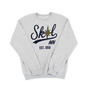 A light heather gray crewneck sweatshirt featuring a navy blue graphic on the chest that reads 'Skol MN EST. 1858' with a gold compass star detail, laid flat against a white background.