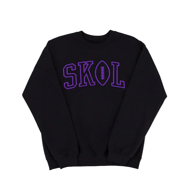 A black crewneck sweatshirt featuring the word 'SKOL' printed across the chest in purple varsity-style block letters, with the letter 'O' designed as a football.