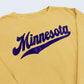 Closeup of a mustard yellow sweatshirt with Minnesota and an athletic swoosh underneath, set against a white background.