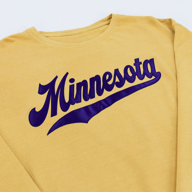 Closeup of a mustard yellow sweatshirt with Minnesota and an athletic swoosh underneath, set against a white background.