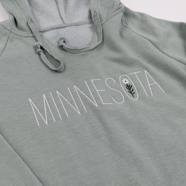 Sage green hoodie with 'MINNESOTA' text and a wildflower on a white background