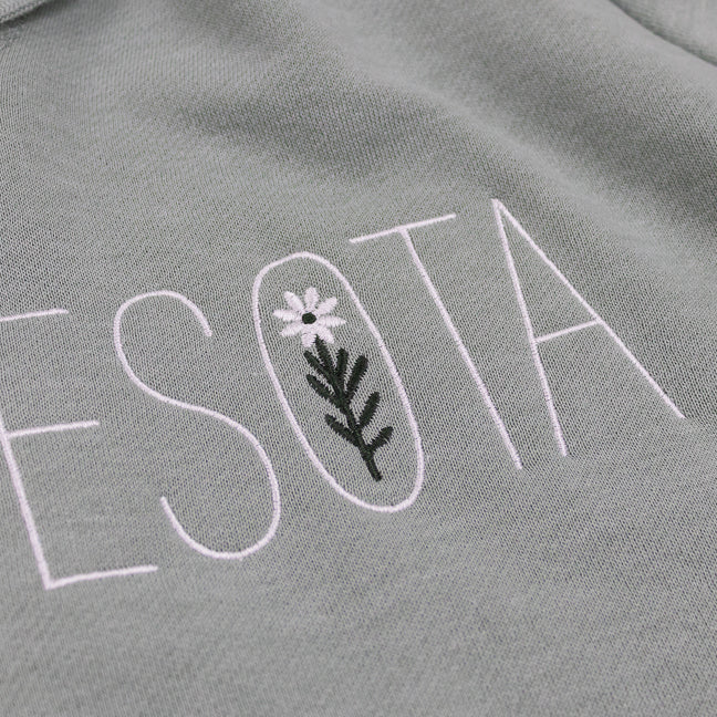 Embroidered text on a sage green fabric with floral design