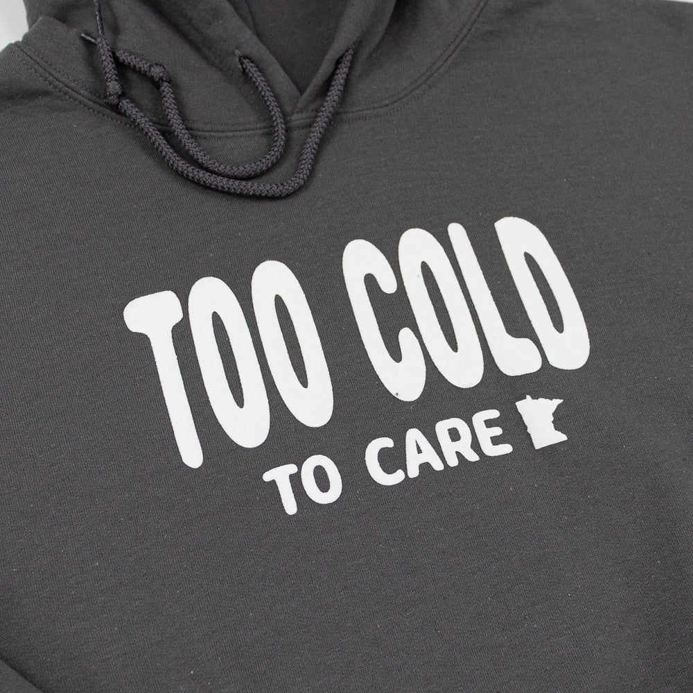 Gray hooded sweatshirt with white bubble font that reads "Too Cold to Care" across the front in white. 