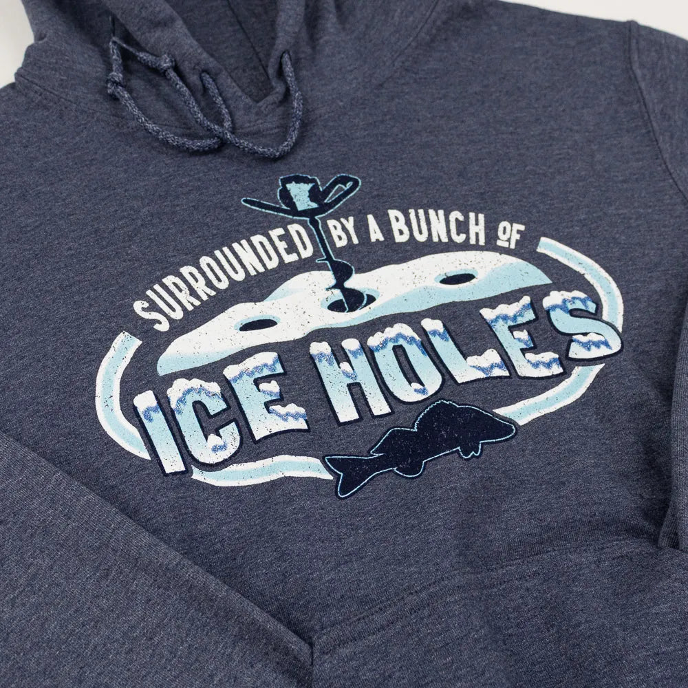 Blue/grey hooded sweatshirt with a wintry ice fishing scene and text that reads "Surrounded by a bunch of ice holes" against a white background.