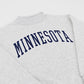Close-up of a light heather gray sweatshirt with the word 'MINNESOTA' printed across the chest in dark navy blue varsity-style lettering.