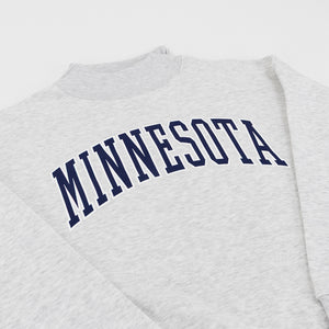 Close-up of a light heather gray sweatshirt with the word 'MINNESOTA' printed across the chest in dark navy blue varsity-style lettering.