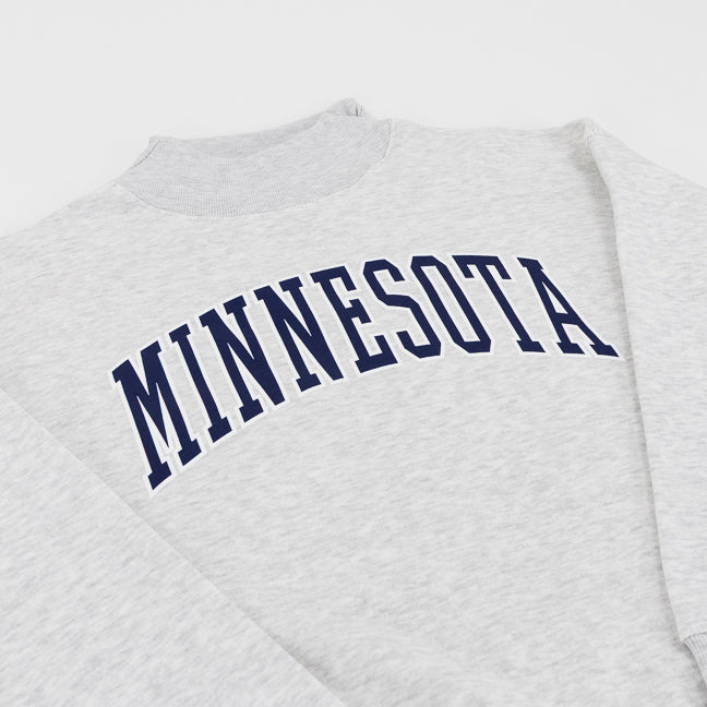 Close-up of a light heather gray sweatshirt with the word 'MINNESOTA' printed across the chest in dark navy blue varsity-style lettering.
