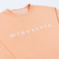 Peach-colored sweatshirt with 'minnesota' text on a white background
