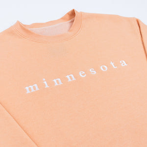 Peach-colored sweatshirt with 'minnesota' text on a white background