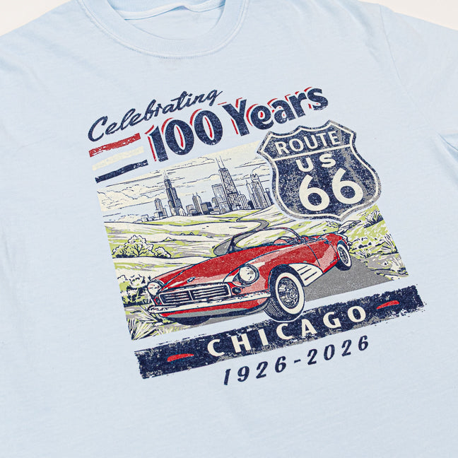 Light blue t-shirt with a graphic of a red car, Route 66 sign, and text celebrating 100 years on a beige background.