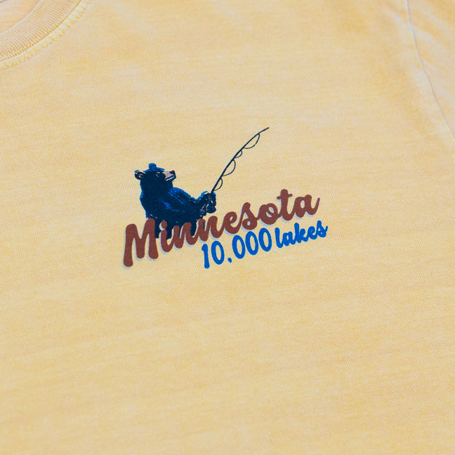 Design of a bear fishing and Minnesota 10,000 Lakes text on a mustard yellow t-shirt.