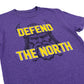 A close-up of a purple heather t-shirt featuring a graphic of a Viking warrior with the text 'DEFEND THE NORTH' in bold yellow letters with white outlines.