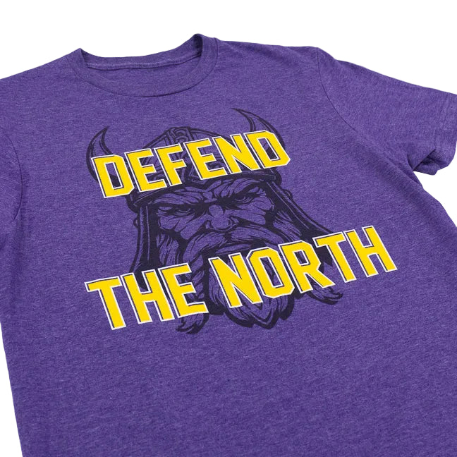 A close-up of a purple heather t-shirt featuring a graphic of a Viking warrior with the text 'DEFEND THE NORTH' in bold yellow letters with white outlines.