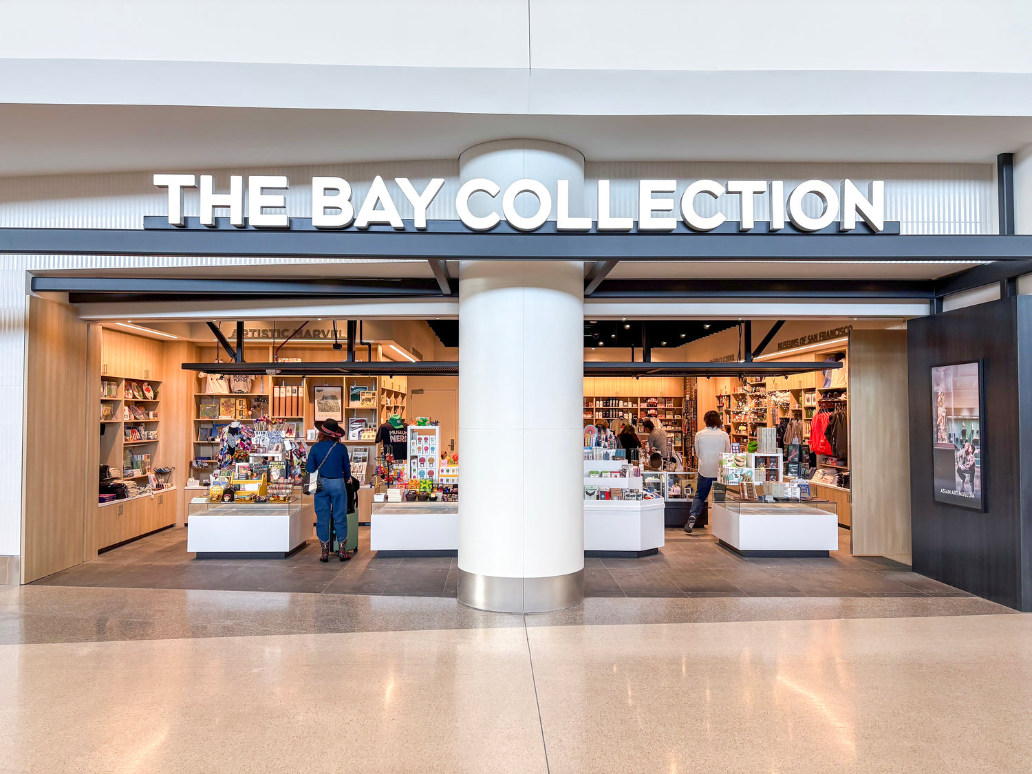 Storefront of 'The Bay Collection' with people inside, large sign above entrance.