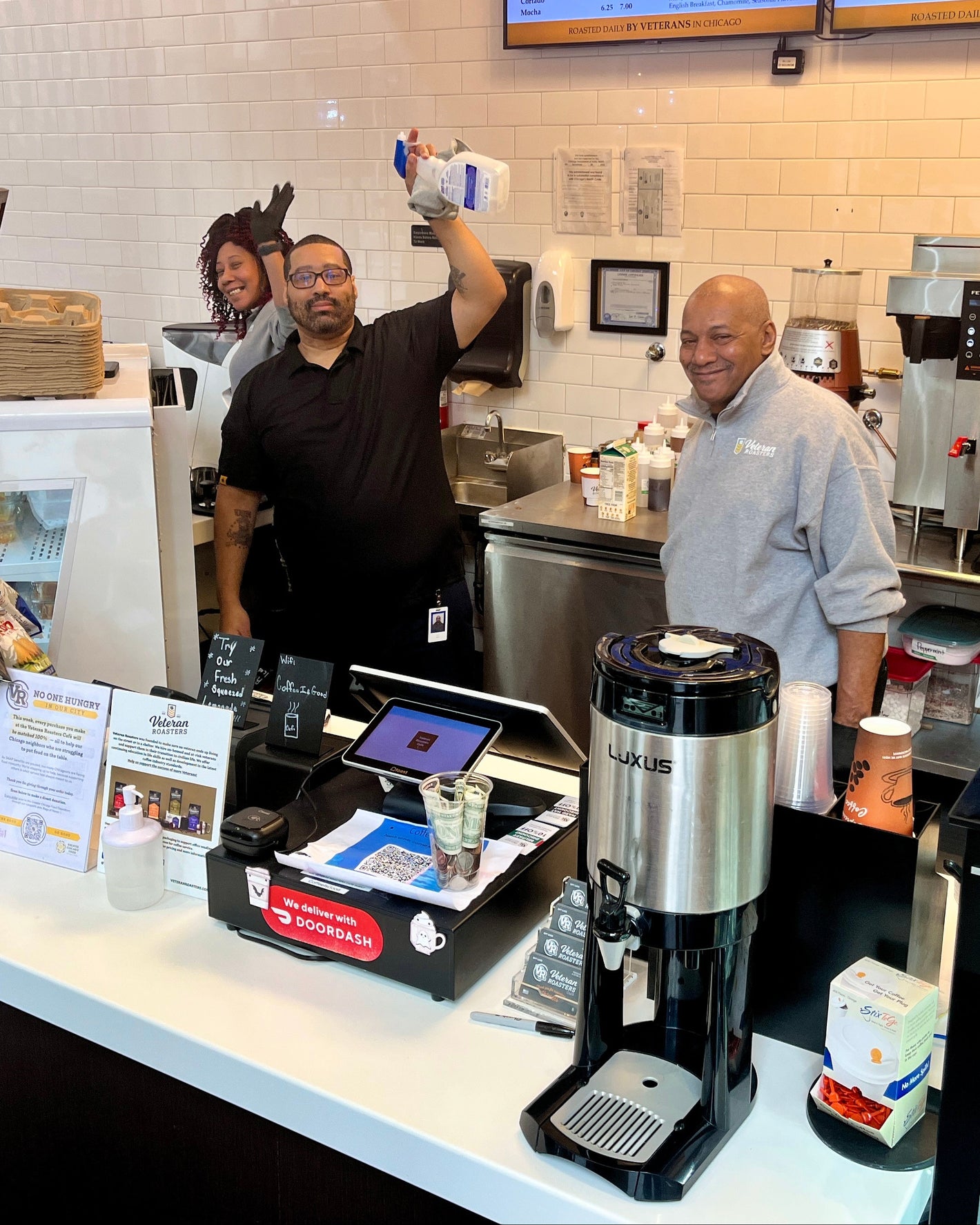 People working behind a counter in a coffee shop with various equipment and supplies.